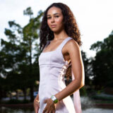 Woman in a light-colored dress posing beside a pond during golden hour.