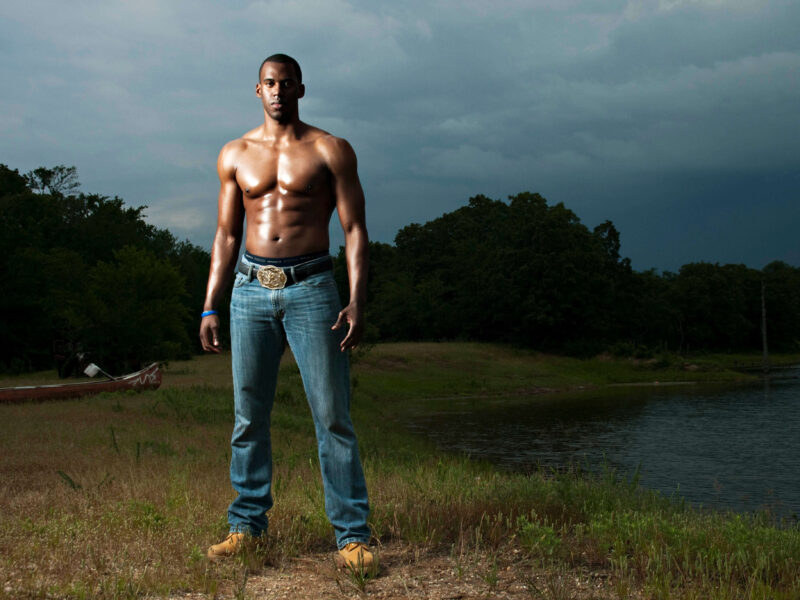 Outdoor portrait of a man standing beside a lake beneath dark storm clouds, illuminated with dramatic off-camera lighting.
