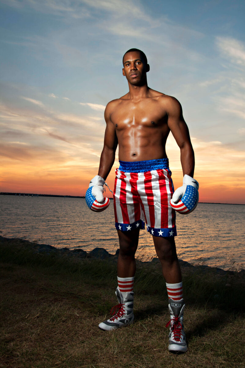 Portrait of a boxer wearing patriotic boxing shorts and gloves standing along a lakeshore during sunset.