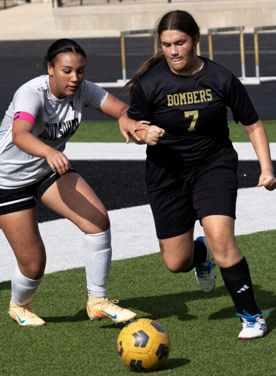 Midwest City middle school girls soccer player in black uniform dribbling the ball while being challenged by a defender