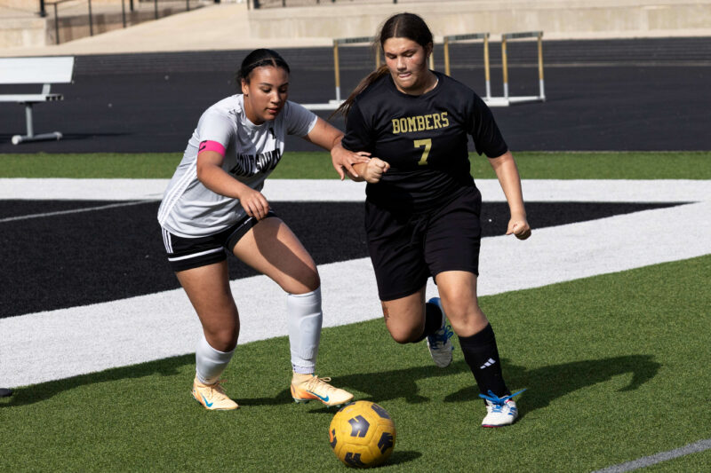 Midwest City middle school girls soccer player in black uniform dribbling the ball while being challenged by a defender