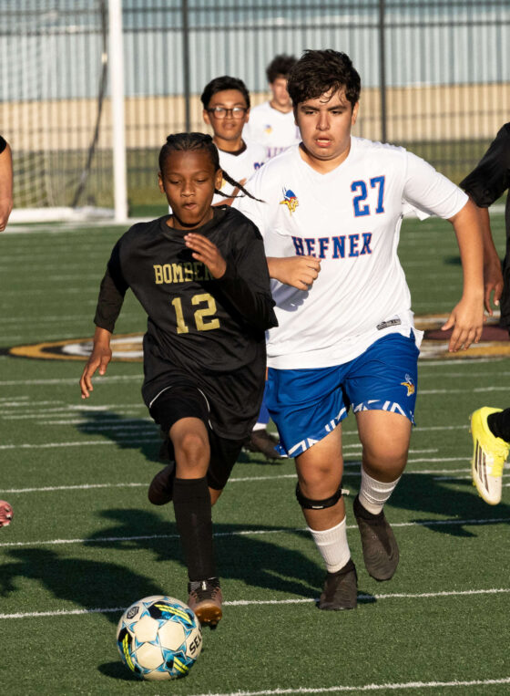Midwest City Bombers soccer players sprinting toward the ball against Hefner player during a competitive boys match