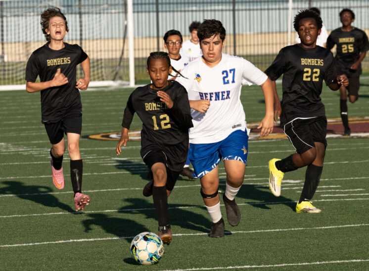 Midwest City Bombers soccer players sprinting toward the ball against Hefner player during a competitive boys match