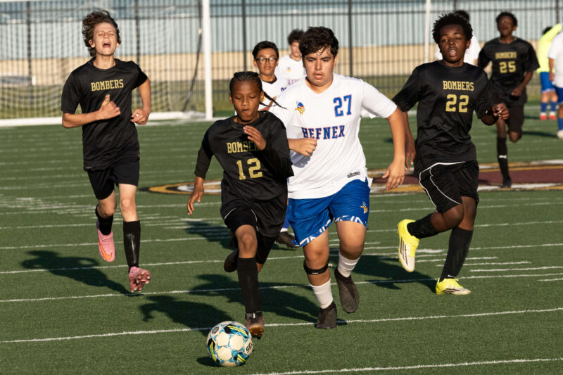 Midwest City Bombers soccer players sprinting toward the ball against Hefner player during a competitive boys match