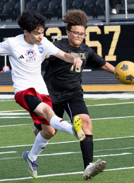 Midwest City middle school boys soccer player in black challenges a Dove Academy player for the ball during a match