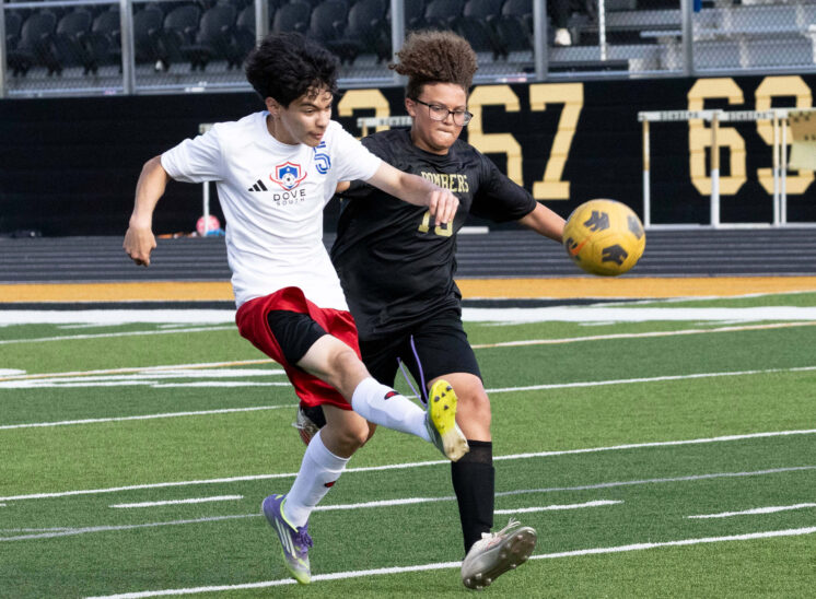 Midwest City middle school boys soccer player in black challenges a Dove Academy player for the ball during a match