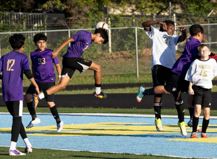 youth soccer player heading ball while defender challenges Oklahoma sports photography