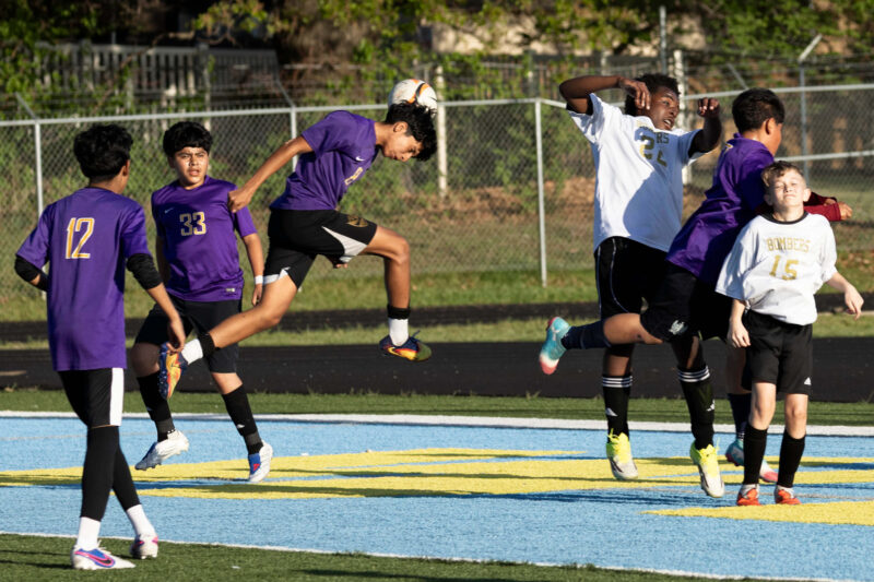 youth soccer player heading ball while defender challenges Oklahoma sports photography