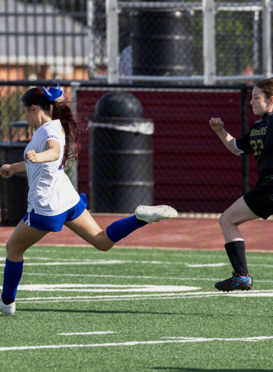 Midwest City Bombers girls soccer player sprinting with the ball while a Bomber defender chases during a match