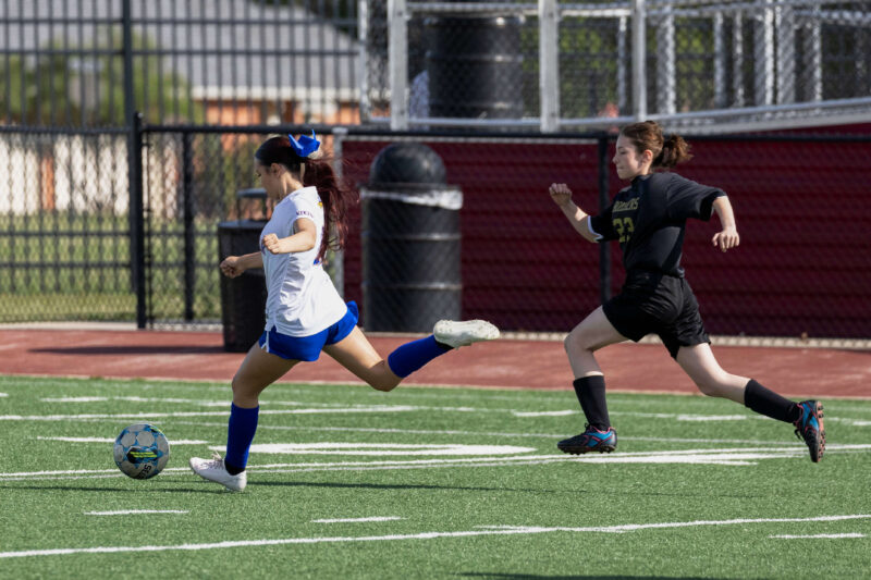 Midwest City Bombers girls soccer player sprinting with the ball while a Bomber defender chases during a match