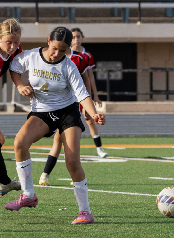 Midwest City middle school girls soccer player in white shields the ball from a PC Capps defender in red and black
