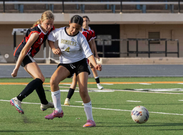 Midwest City middle school girls soccer player in white shields the ball from a PC Capps defender in red and black