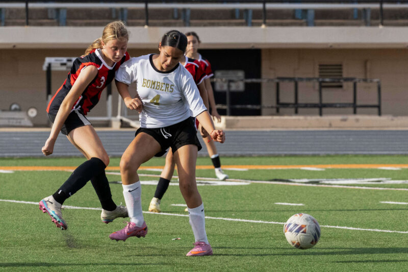 Midwest City middle school girls soccer player in white shields the ball from a PC Capps defender in red and black