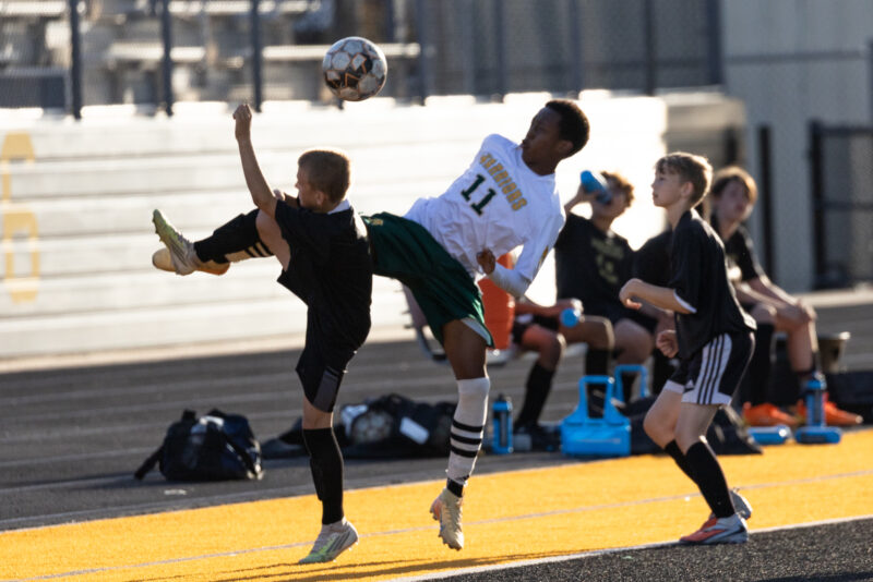 Midwest City middle school boys soccer players in black challenge a Western Oaks player in white for an airborne ball