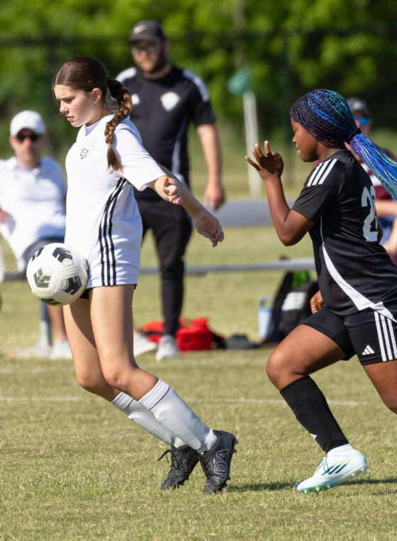 A Midwest City Vision player in white controls the ball while a Western Oklahoma FC defender in black closes in during a U15 Girls tournament soccer match at GRC-Norman.