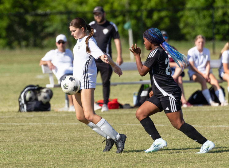A Midwest City Vision player in white controls the ball while a Western Oklahoma FC defender in black closes in during a U15 Girls tournament soccer match at GRC-Norman.