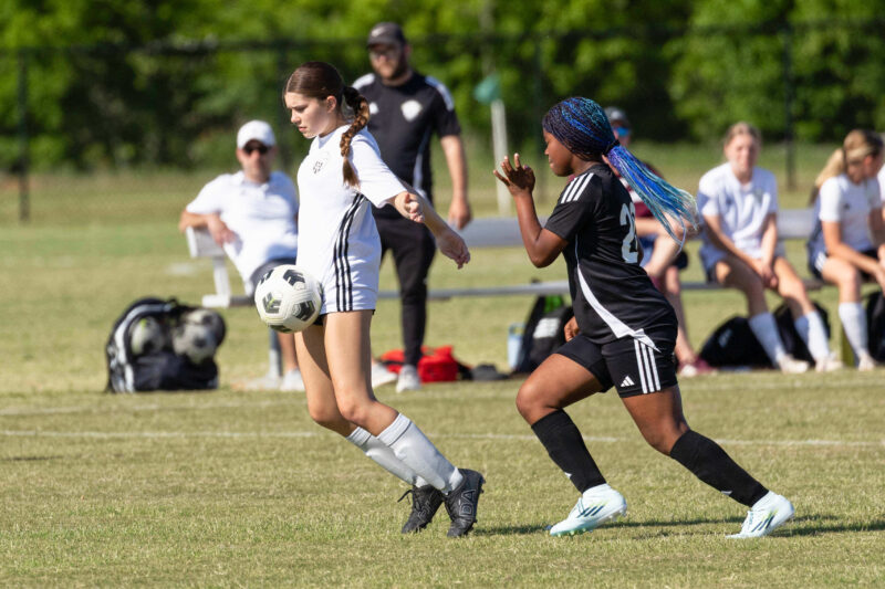 A Midwest City Vision player in white controls the ball while a Western Oklahoma FC defender in black closes in during a U15 Girls tournament soccer match at GRC-Norman.