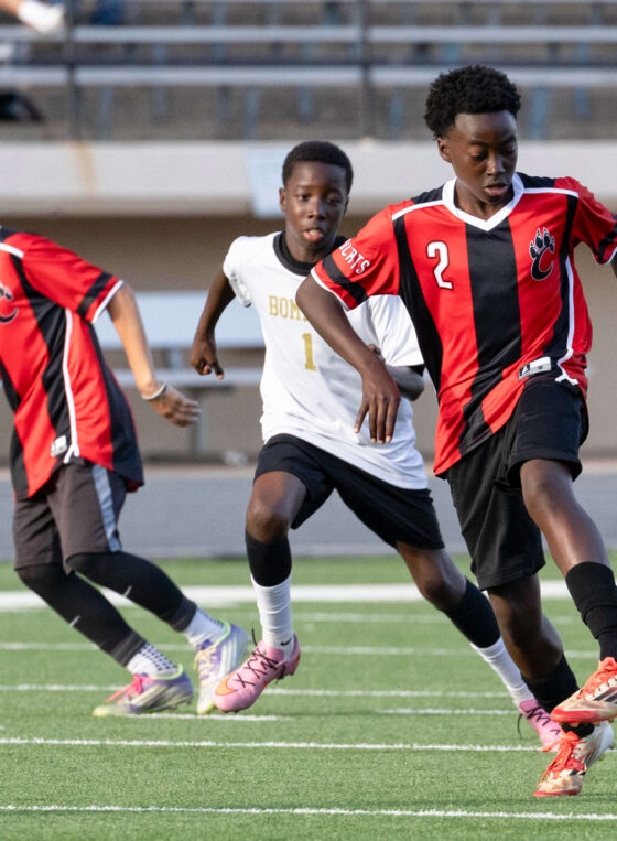 Midwest City middle school boys soccer player in white chases a PC Capps player in red and black during a match