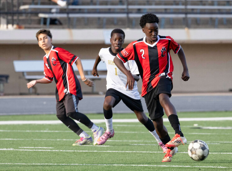 Midwest City middle school boys soccer player in white chases a PC Capps player in red and black during a match