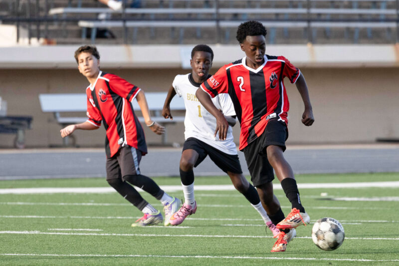 Midwest City middle school boys soccer player in white chases a PC Capps player in red and black during a match