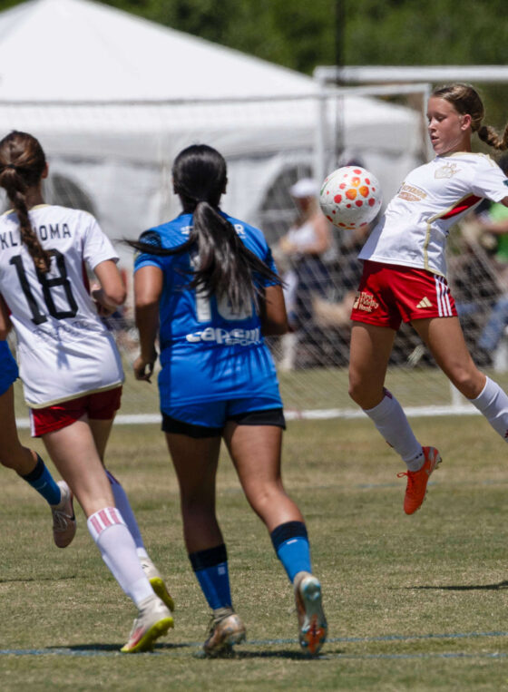 U16 girls soccer player from Oklahoma Energy in white jumps to control the ball while Amarillo Rush defenders in blue close in during the 2026 NOKC Spring Finale