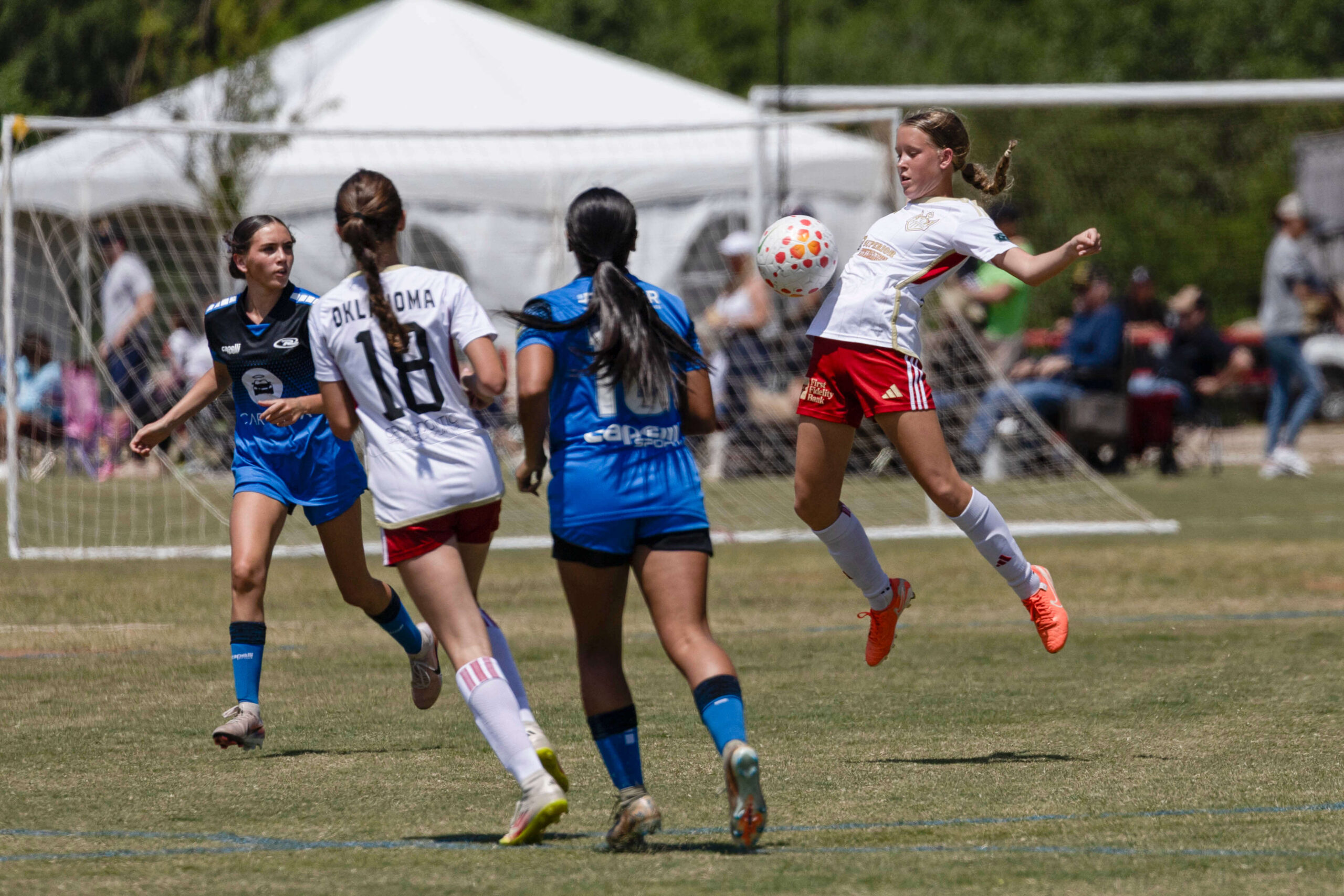 U16 girls soccer player from Oklahoma Energy in white jumps to control the ball while Amarillo Rush defenders in blue close in during the 2026 NOKC Spring Finale
