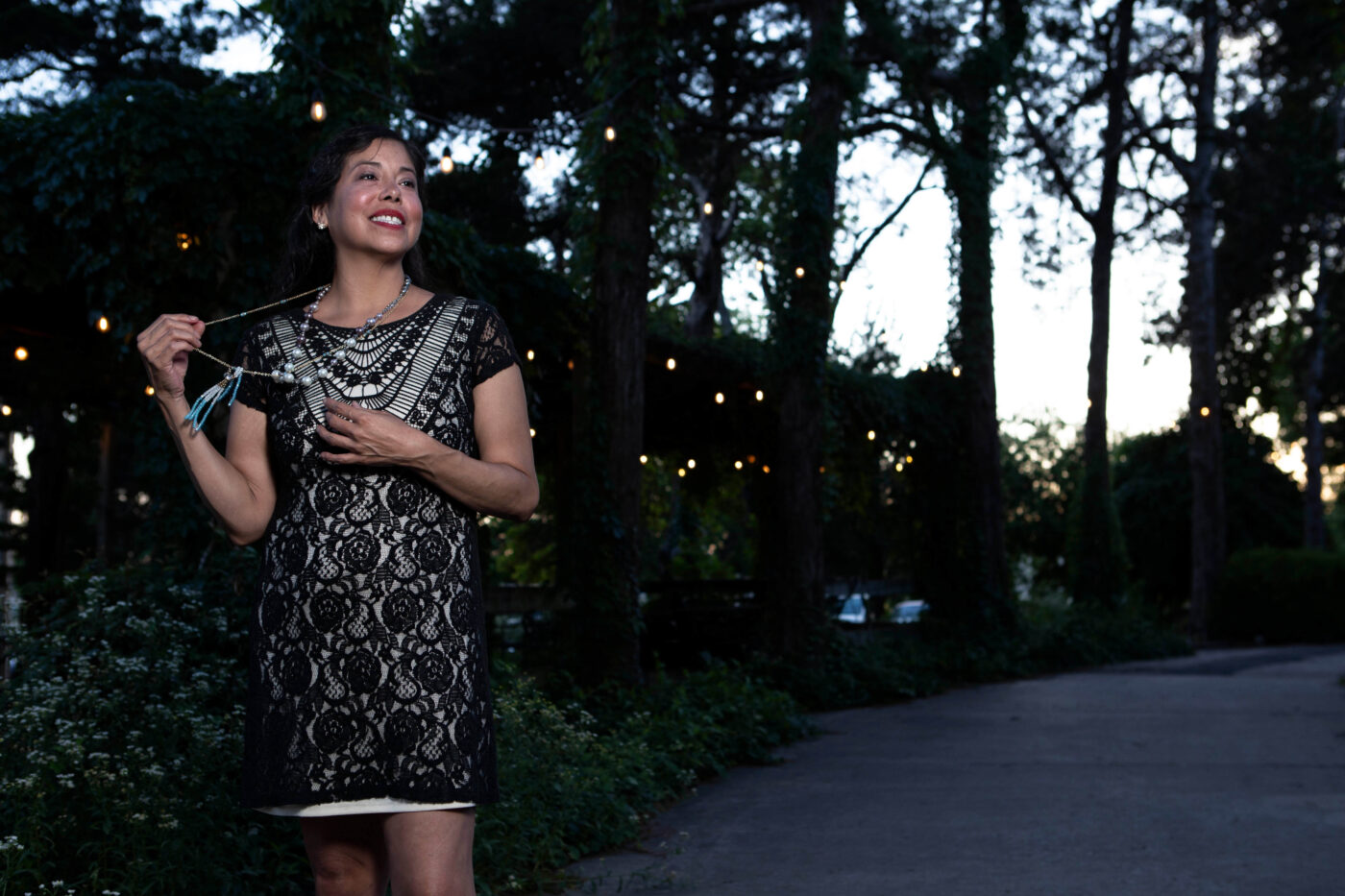 Woman in a black lace vintage-style dress posing outdoors beneath string lights at Castle Falls during a 1940s-themed photomeet.