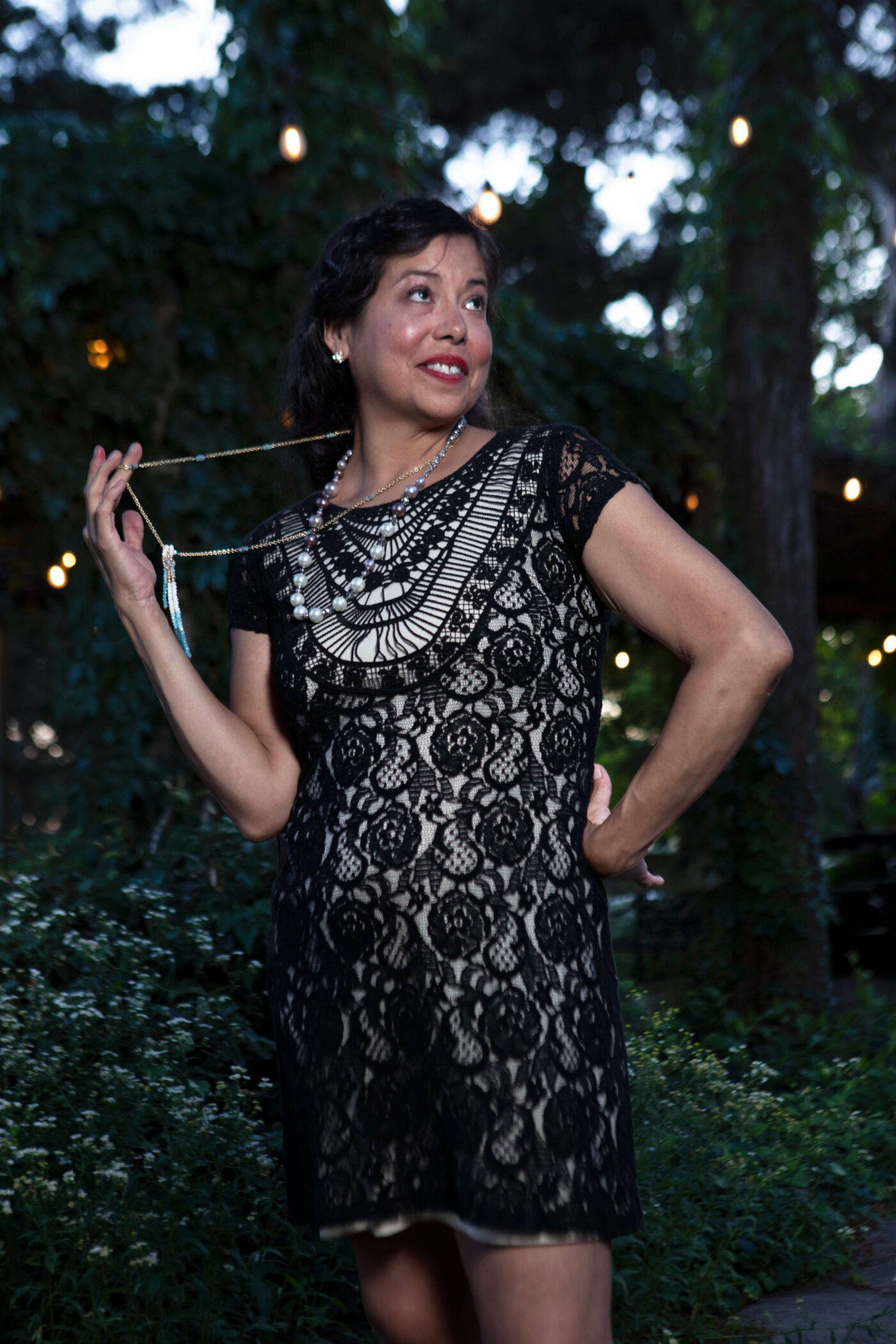 Close portrait of a woman wearing a black lace dress and vintage jewelry posing outdoors at dusk during a 1940s-themed photomeet.