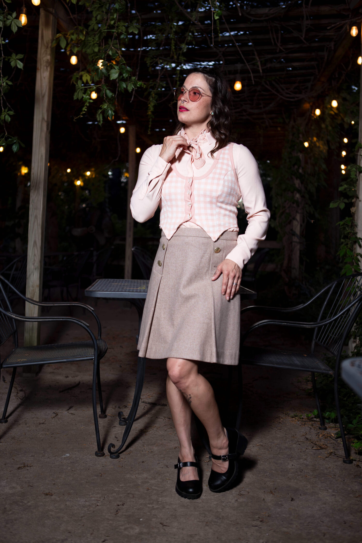 Portrait of Gema Khaos posing beneath hanging string lights at Castle Falls during a 1940s-themed photomeet, wearing a pastel vintage-inspired outfit and round pink glasses.
