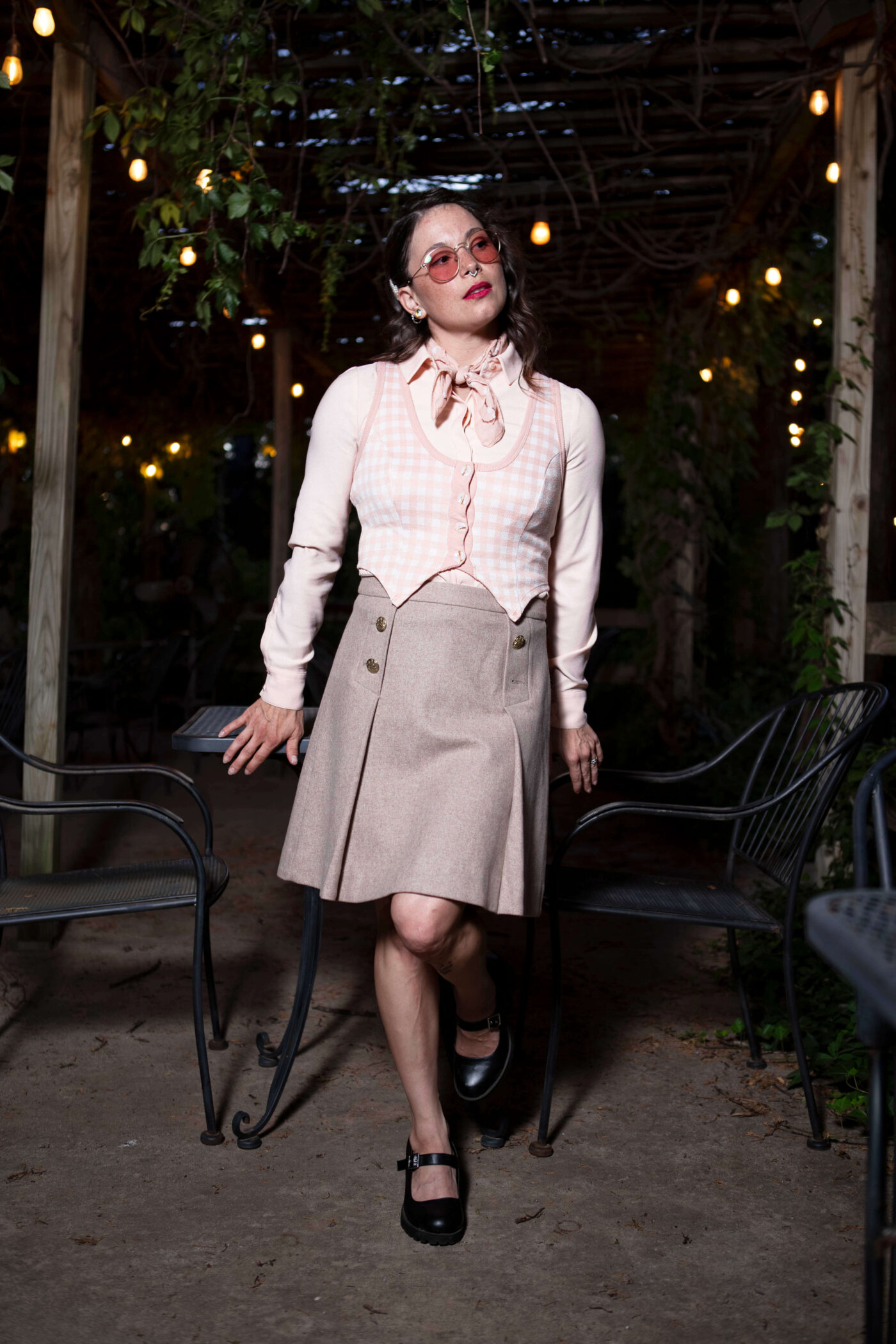 Gema Khaos posing in a vintage-inspired outfit between outdoor café tables beneath glowing lights at Castle Falls during a themed photography event.