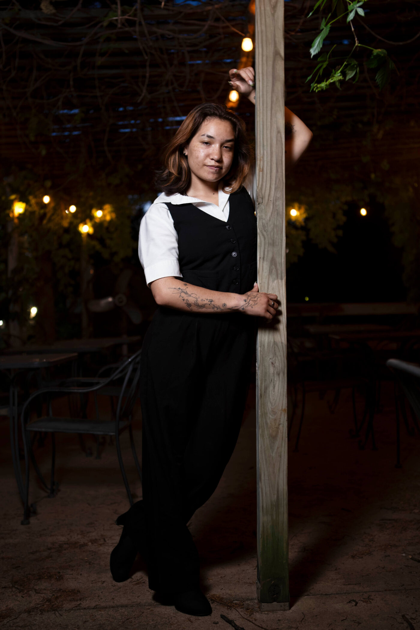 Model toxicwoman55 leaning against a wooden post under string lights at Castle Falls during a vintage-themed 1940s photomeet.