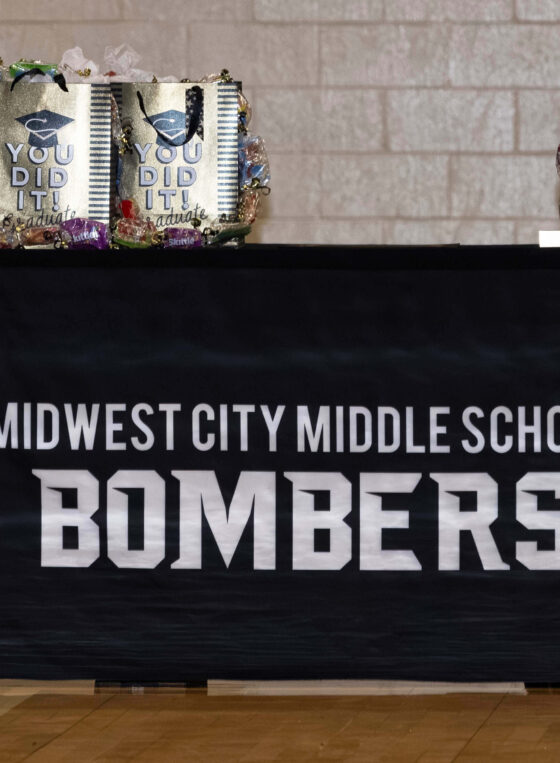 Table display at the Midwest City Middle School Bridging Ceremony featuring “Midwest City Middle School Bombers” branding and graduation gift bags prepared for students transitioning to high school.