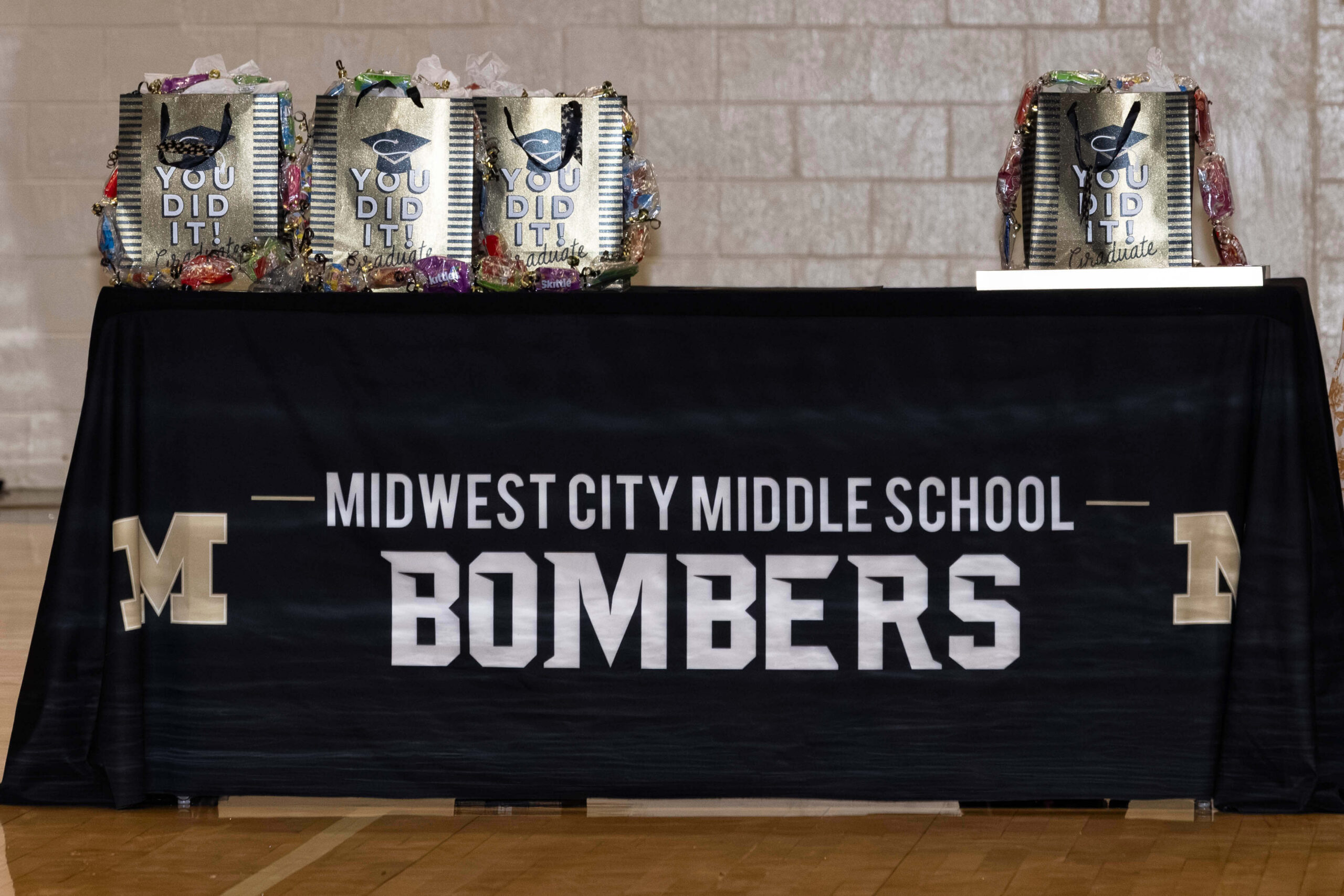 Table display at the Midwest City Middle School Bridging Ceremony featuring “Midwest City Middle School Bombers” branding and graduation gift bags prepared for students transitioning to high school.