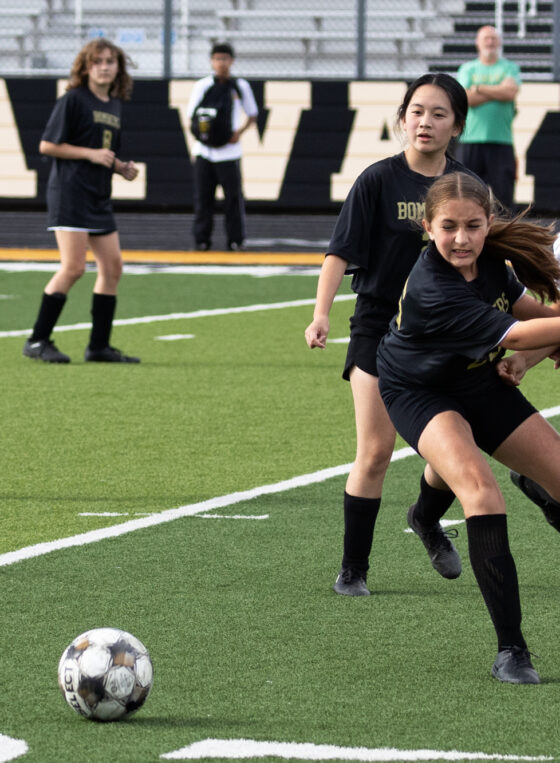 Midwest City middle school girls soccer player in black sprints to the ball ahead of a Western Oaks player in white