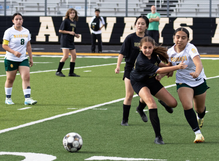 Midwest City middle school girls soccer player in black sprints to the ball ahead of a Western Oaks player in white