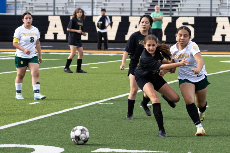 Midwest City middle school girls soccer player in black sprints to the ball ahead of a Western Oaks player in white