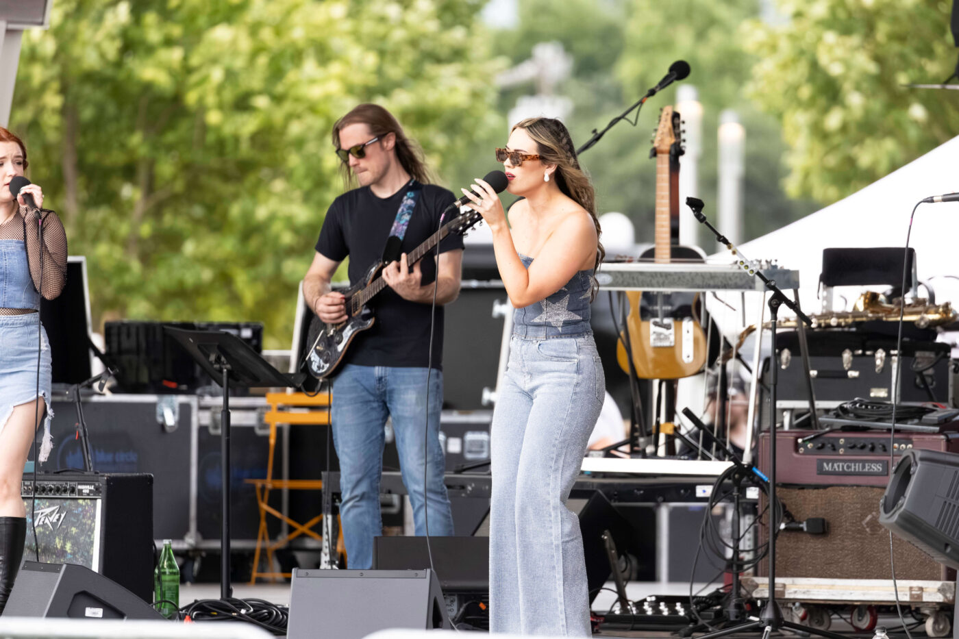 Female vocalist from OK3 sings into a microphone during an outdoor concert at Scissortail Park.