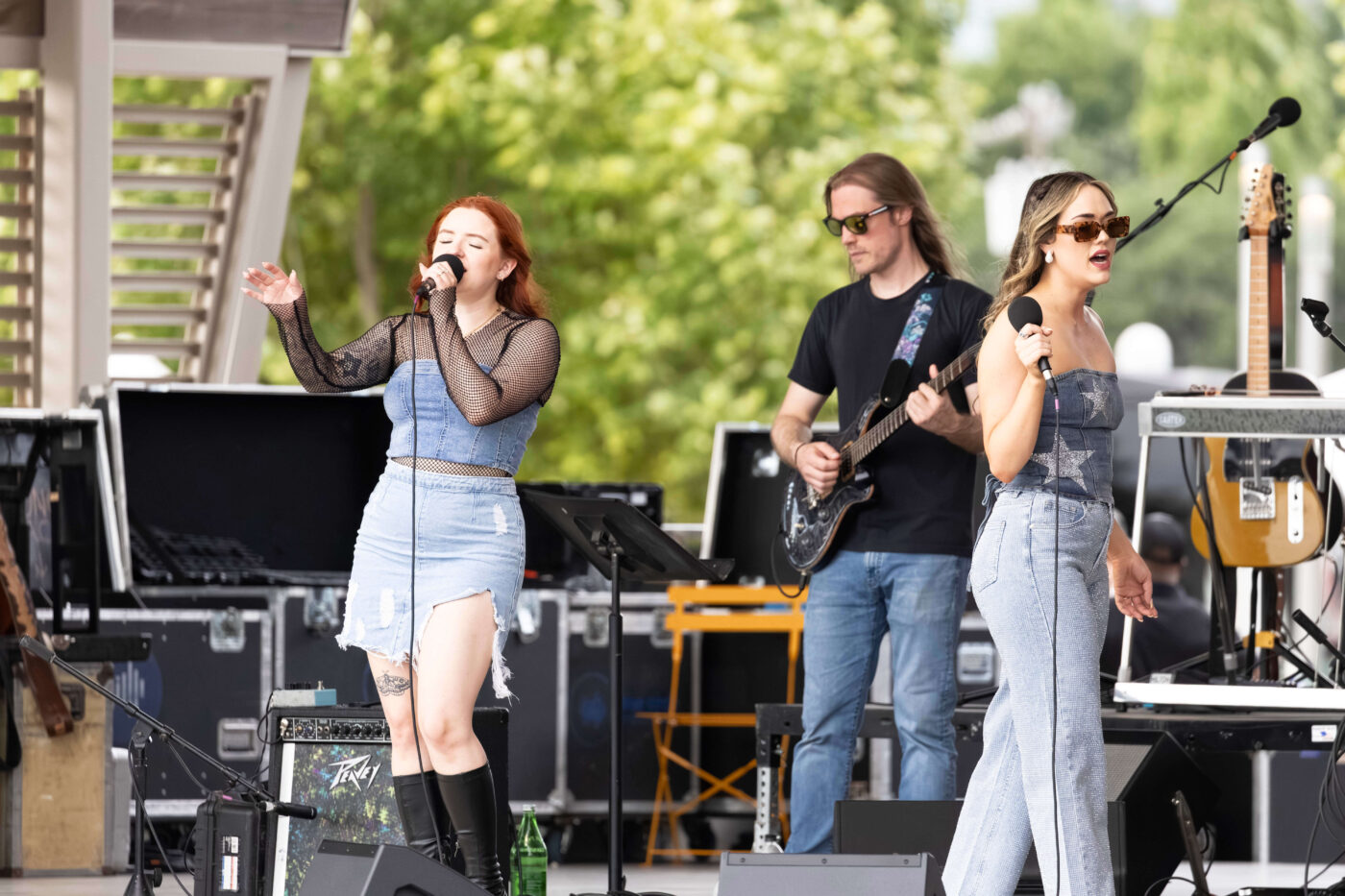 Two vocalists and a guitarist from OK3 perform together on stage at Scissortail Park.