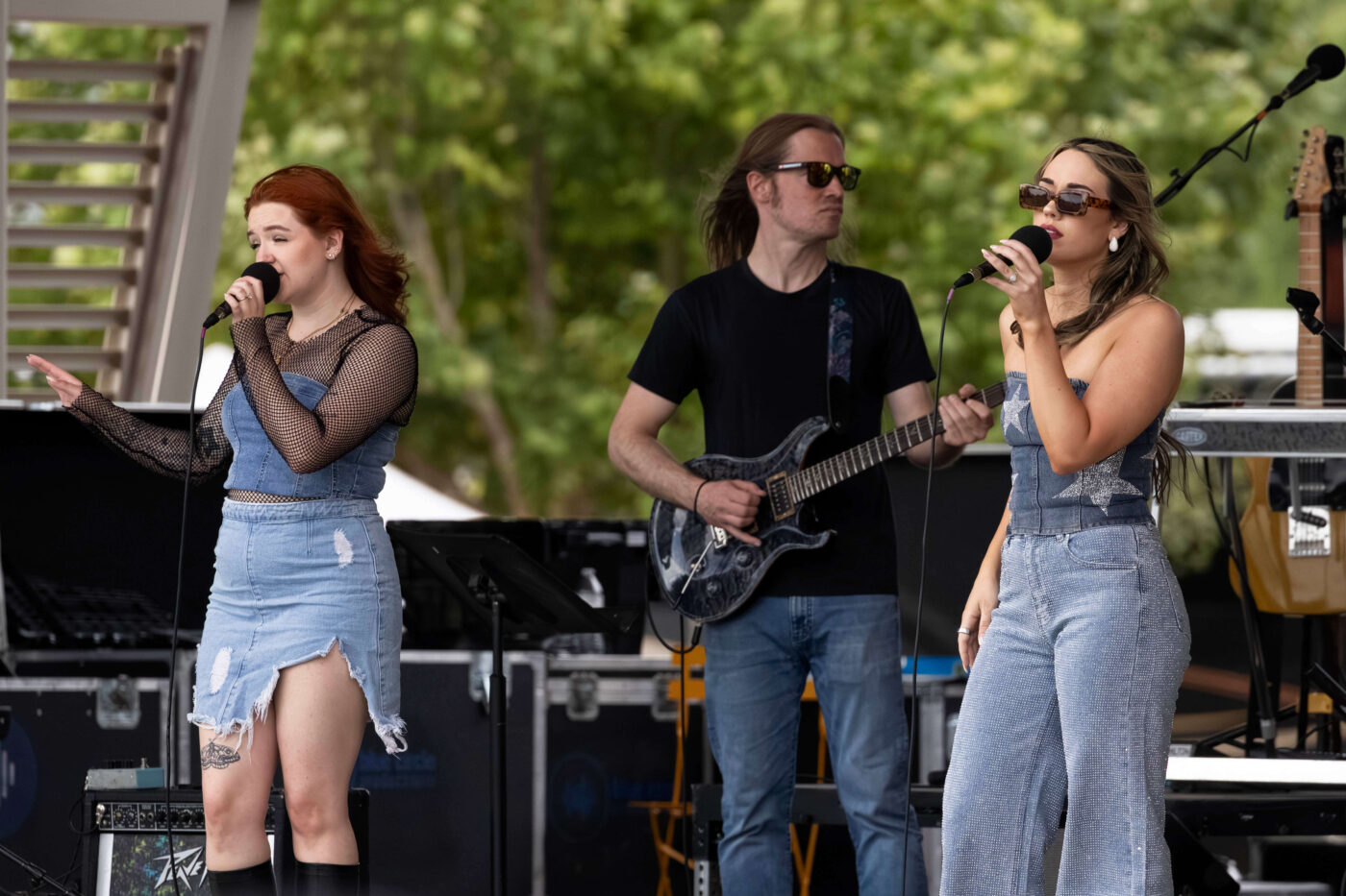 Two OK3 vocalists perform with a guitarist during an evening concert at Scissortail Park.