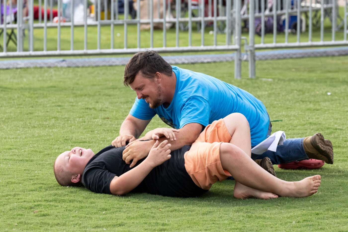 A father and son laugh while playing together on the grass at Scissortail Park during the Route 66 Centennial Celebration.