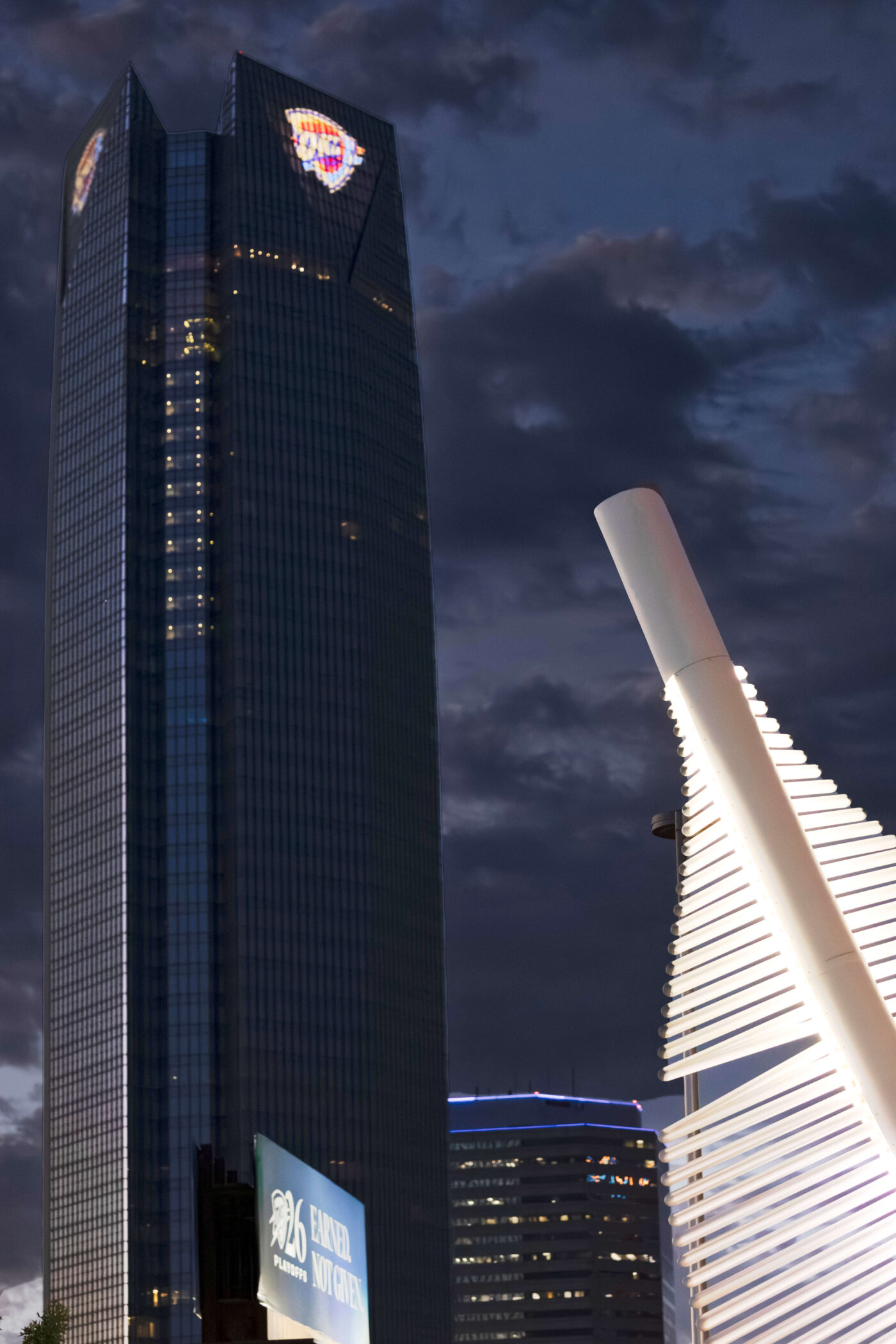Devon Tower rises above downtown Oklahoma City at dusk with dramatic clouds and illuminated architectural elements in the foreground.