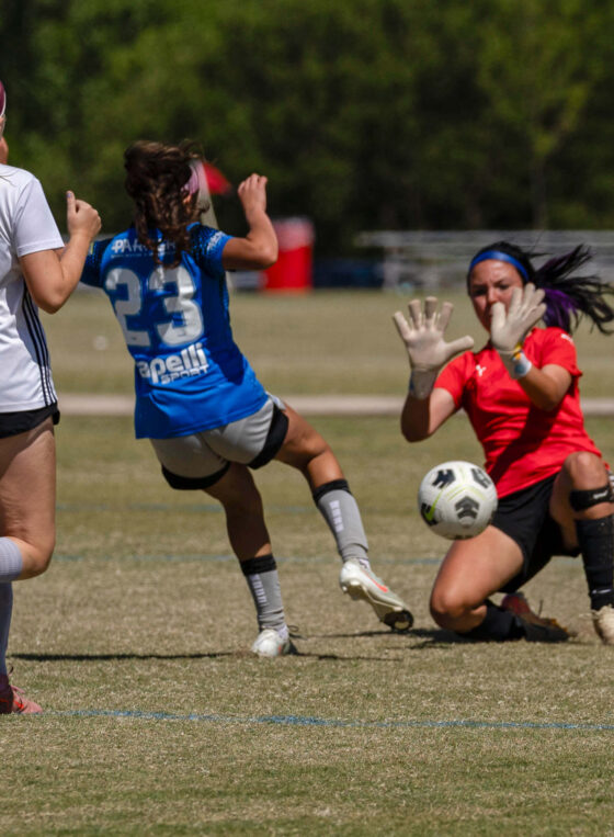 Amarillo Rush attacker in blue attempts a close-range shot as the Midwest City Vision goalkeeper in red makes a save during a U16 Girls Gold Division semifinal match at the 2026 NOKC Spring Finale