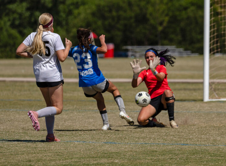 Amarillo Rush attacker in blue attempts a close-range shot as the Midwest City Vision goalkeeper in red makes a save during a U16 Girls Gold Division semifinal match at the 2026 NOKC Spring Finale