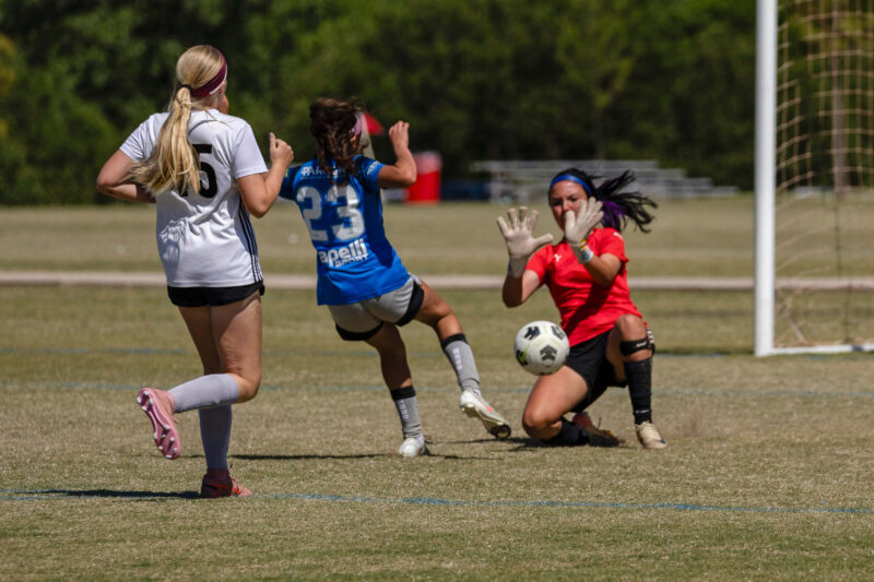 Amarillo Rush attacker in blue attempts a close-range shot as the Midwest City Vision goalkeeper in red makes a save during a U16 Girls Gold Division semifinal match at the 2026 NOKC Spring Finale