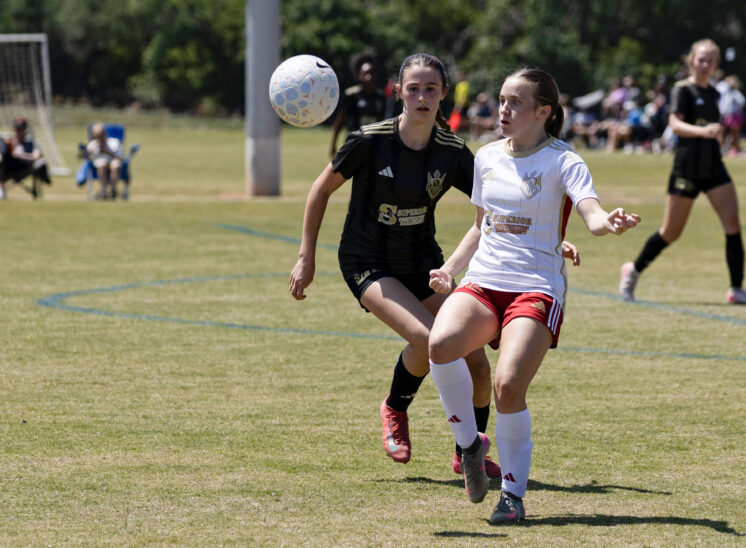 West Side Alliance SC player in white tracks the ball while a Midwest City Vision defender in black closes in during a U16 Girls Gold Division match at the 2026 NOKC Spring Finale