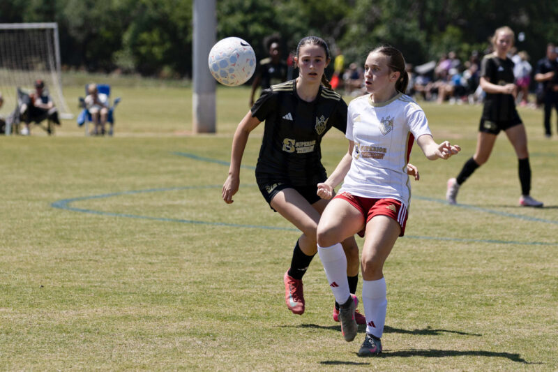 West Side Alliance SC player in white tracks the ball while a Midwest City Vision defender in black closes in during a U16 Girls Gold Division match at the 2026 NOKC Spring Finale