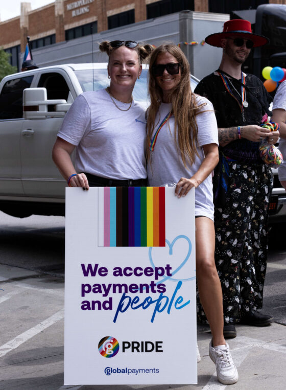 Two parade participants pose with a sign promoting acceptance and inclusion.