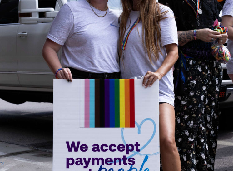 Two parade participants pose with a sign promoting acceptance and inclusion.