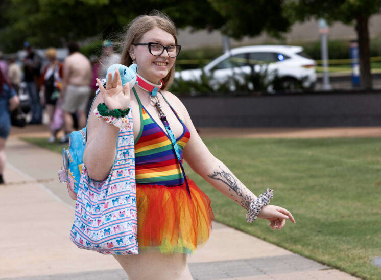 Parade attendee wearing a rainbow-striped outfit waves and smiles while walking during the Oklahoma City Pride Parade.