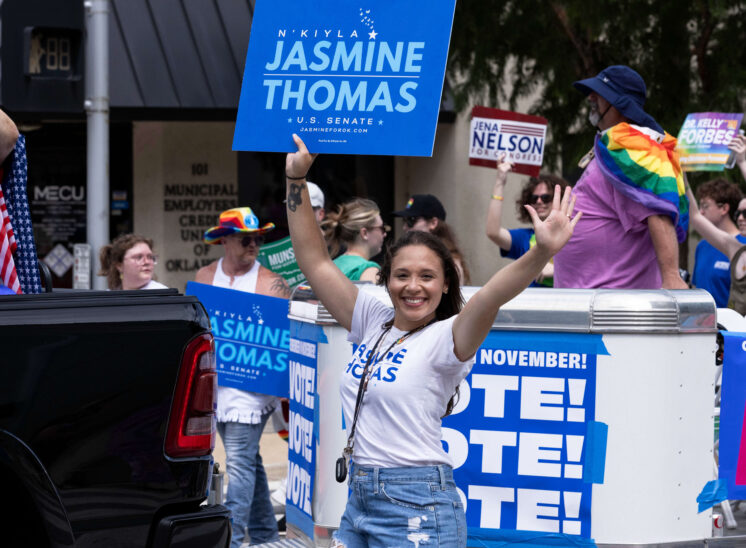 A smiling parade participant waves while walking beside a political campaign float during Oklahoma City Pride.